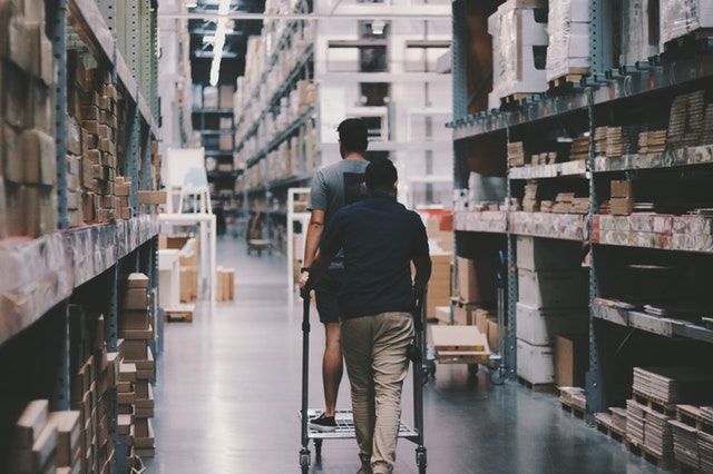 Two men strolling down a warehouse lined with products.